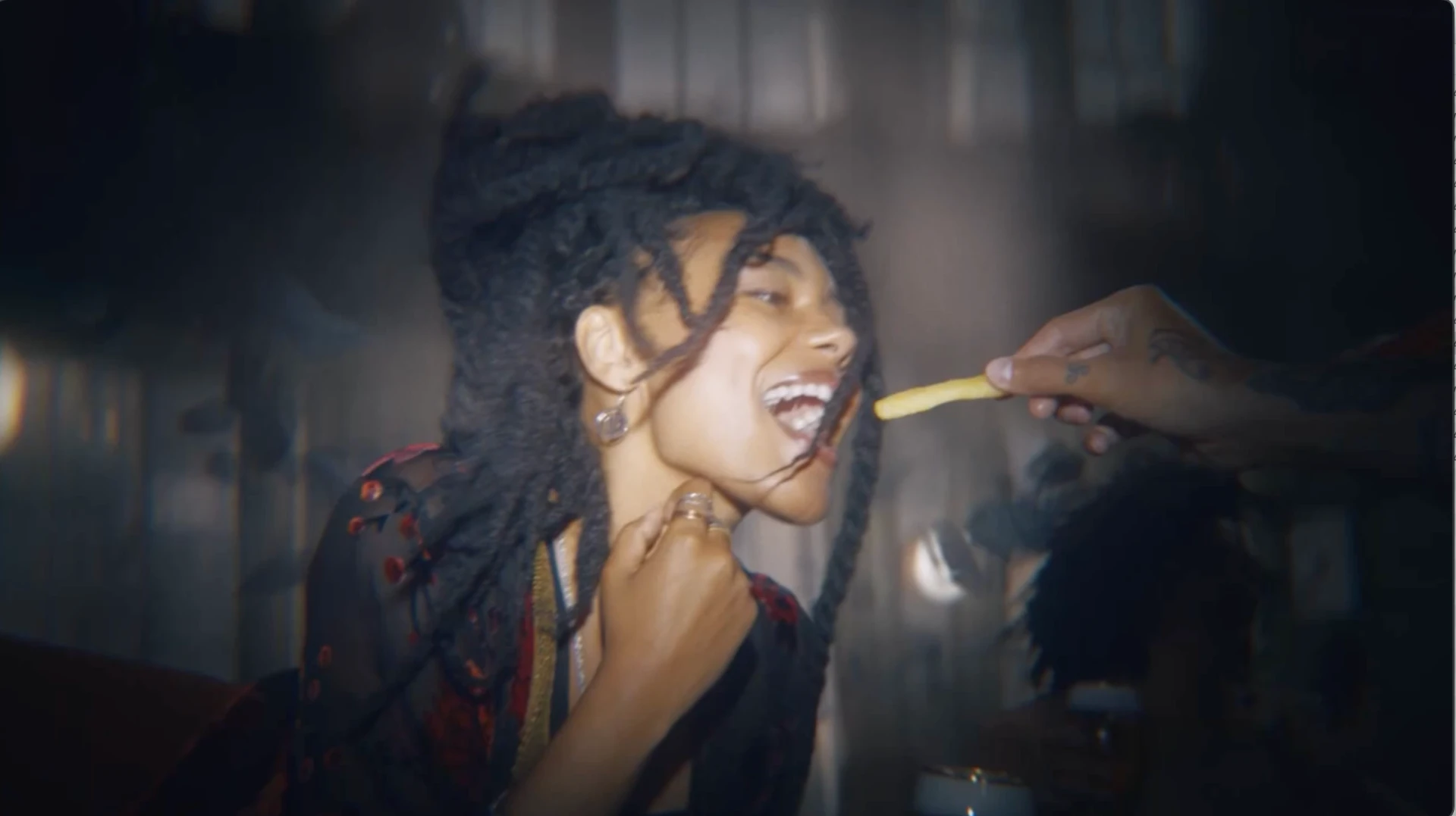 A woman smiling as a french fry is held toward her